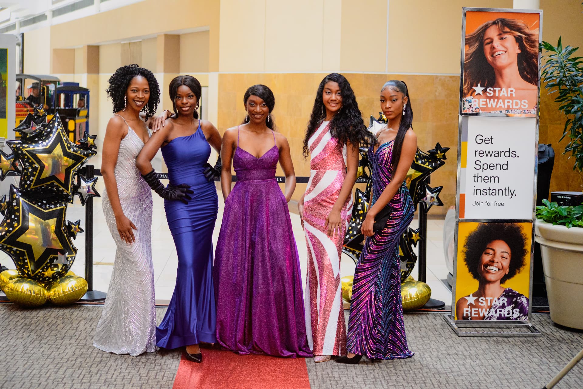Five models in formal gowns posing together on the red carpet at the Macy's 2023 Prom Fashion Show