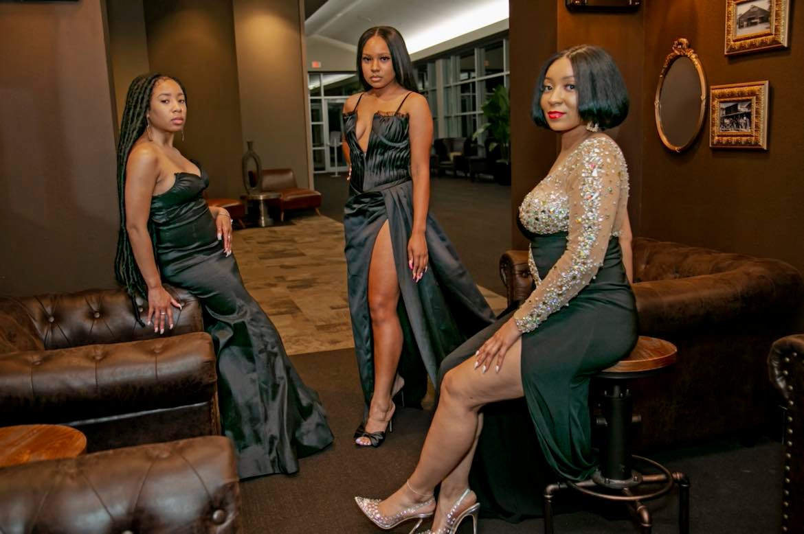 Three young women in black evening gowns posing in a lounge setting